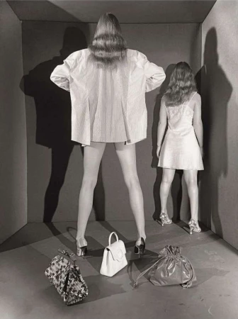 Two models facing a corner in a box set with three handbags on the floor, photographed by Paul Kooiker.