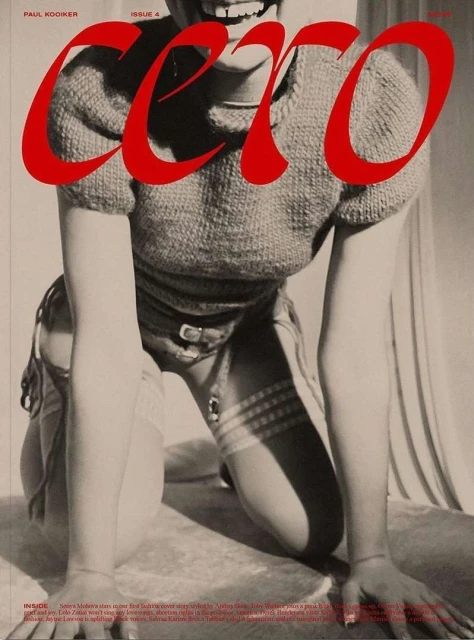 Magazine cover featuring a model kneeling, showcasing a red title, knit sweater, and details of stockings, belt, and a neutral backdrop.