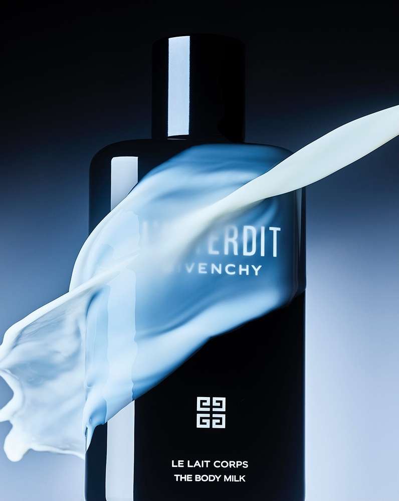A black Givenchy Interdit body milk bottle is in the frame, with a splash of white liquid across the front against a graduated blue background.