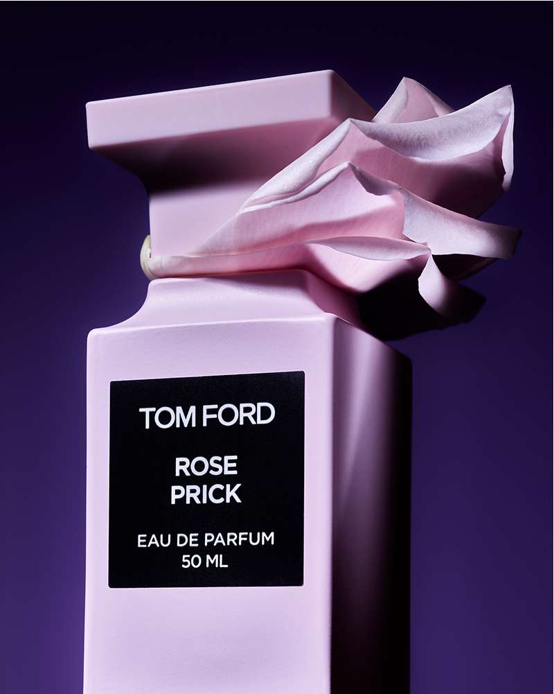 Studio shot of a light-pink Tom Ford Rose Prick Eau de Parfum bottle, wrapped in a pink paper-like material, against a dark-purple background.