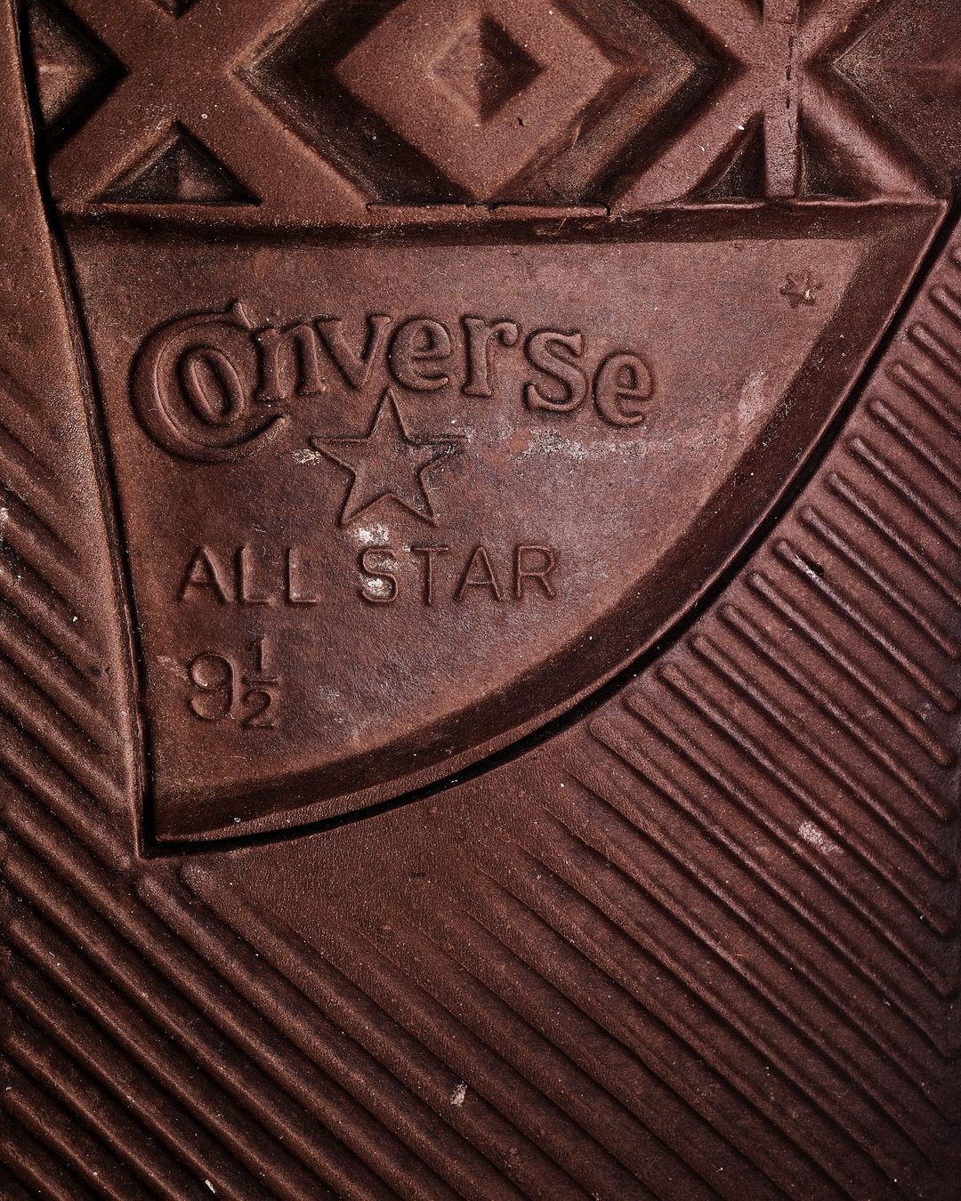 Close-up on the textured brown rubber sole of a Converse All-Star sneaker, featuring the logo and size markings.