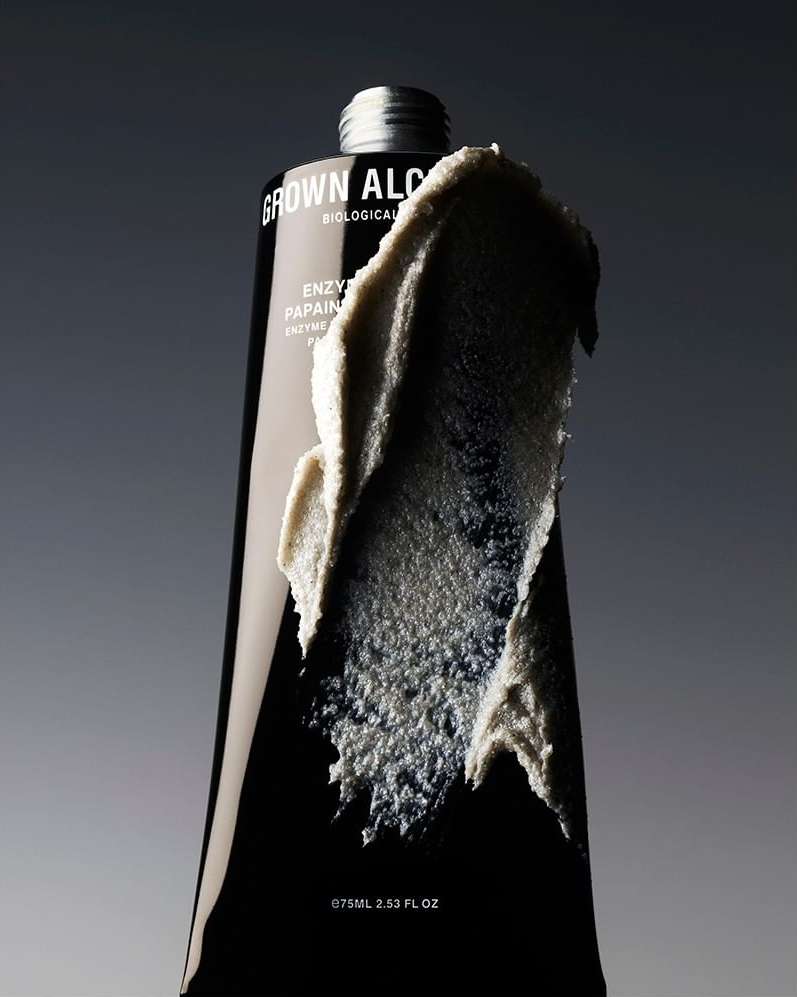 Black tube of Grown Alchemist Enzyme Papain face mask with smear of product on the front, silver cap, grey background.