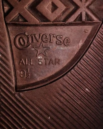 Extreme macro close-up of a brown sneaker sole showing embossed Converse All Star logo and diagonal tread patterns.