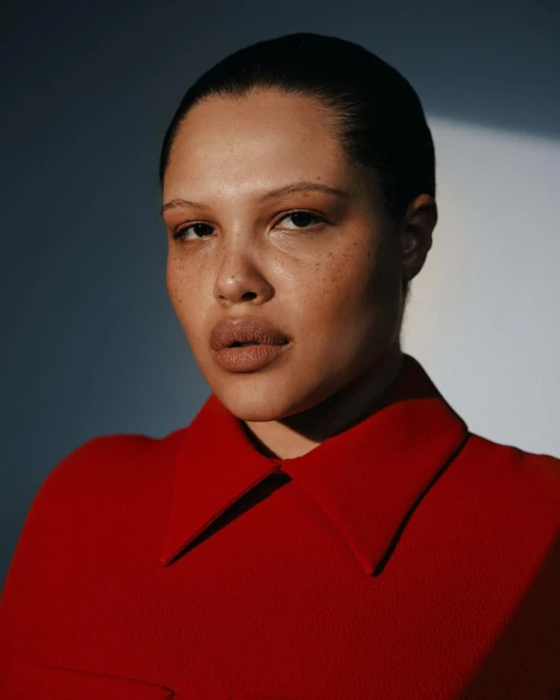Portrait of a woman with freckles wearing a red blouse in a studio with directional lighting, captured in a medium close-up shot.