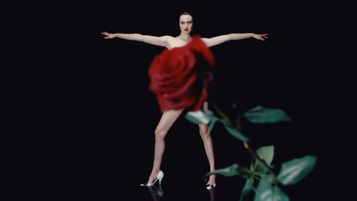 Adult female fashion model in a red rose dress posing in a dark photo studio. Fashion editorial portrait on black backdrop.