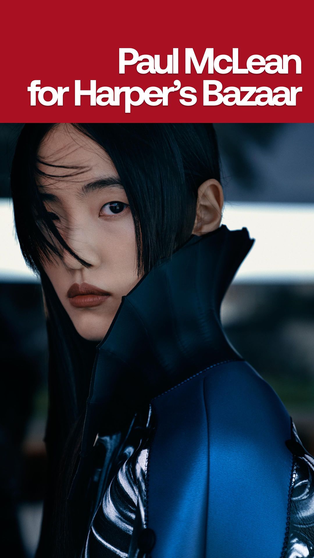 Portrait of an Asian woman with slicked-back black hair wearing a blue and black jacket, set against a dark background. Fashion editorial.