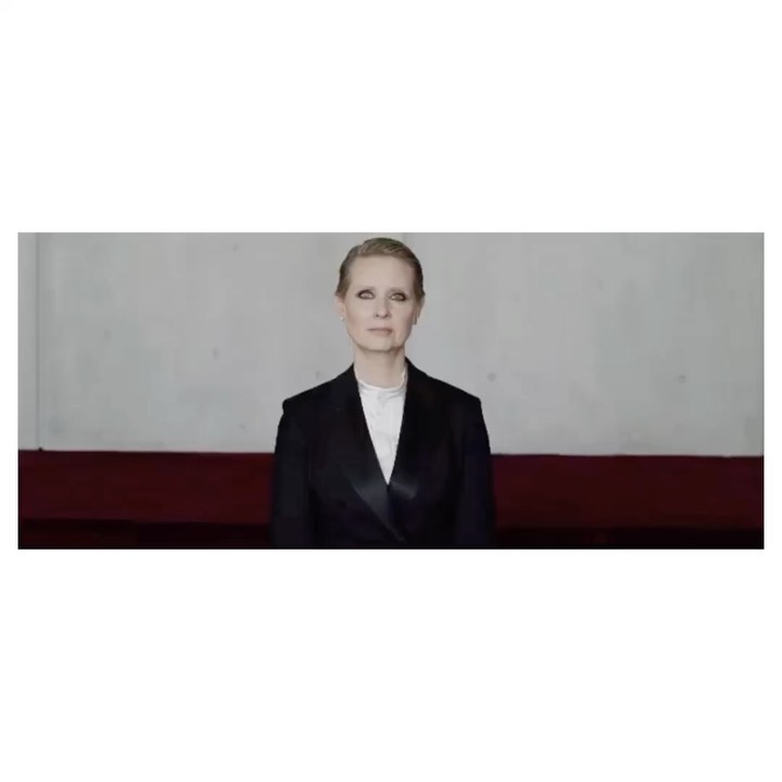 Adult woman in a dark blazer with a white top, looking at the camera with a neutral expression, in front of a two-toned wall.