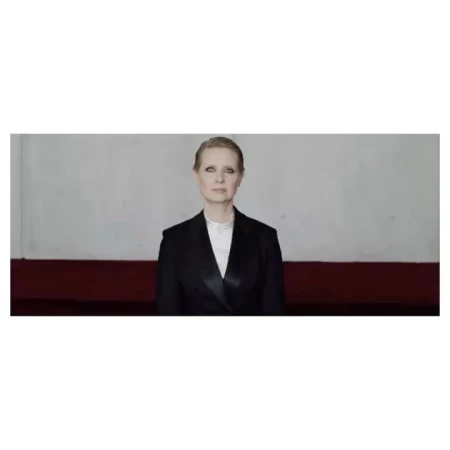 Adult woman in a dark blazer with a white top, looking at the camera with a neutral expression, in front of a two-toned wall.