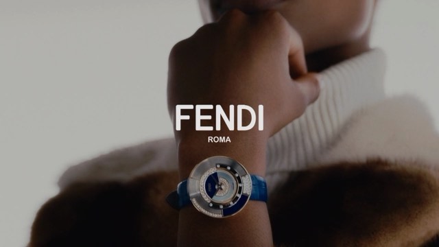 Close-up of a person wearing a Fendi watch, showcasing the brand's logo and elegant design, set against a neutral background.