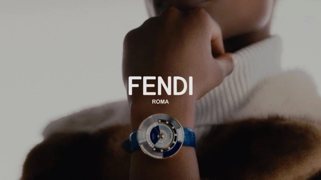 Close-up of a person wearing a Fendi watch, showcasing the brand's logo and elegant design, set against a neutral background.