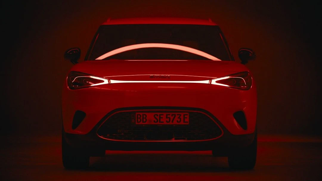 Front view of a red smart car under even lighting, showcasing its modern design and compact form in a dark studio setting.