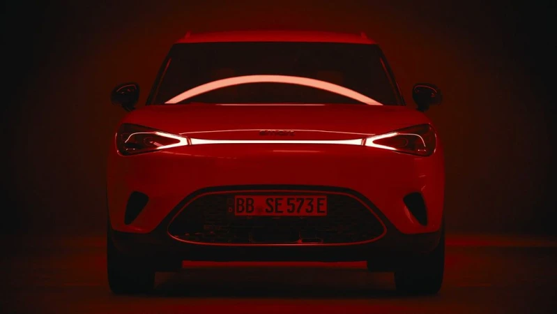 Front view of a red smart car under even lighting, showcasing its modern design and compact form in a dark studio setting.