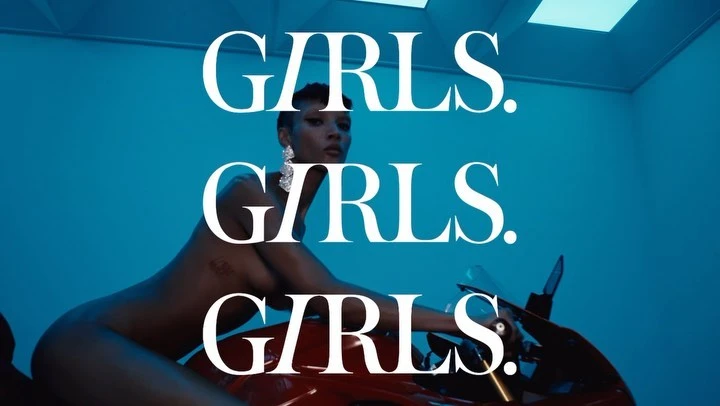 A woman with short hair and large earrings is sitting on a red motorcycle against a blue background with the word GIRLS over her.
