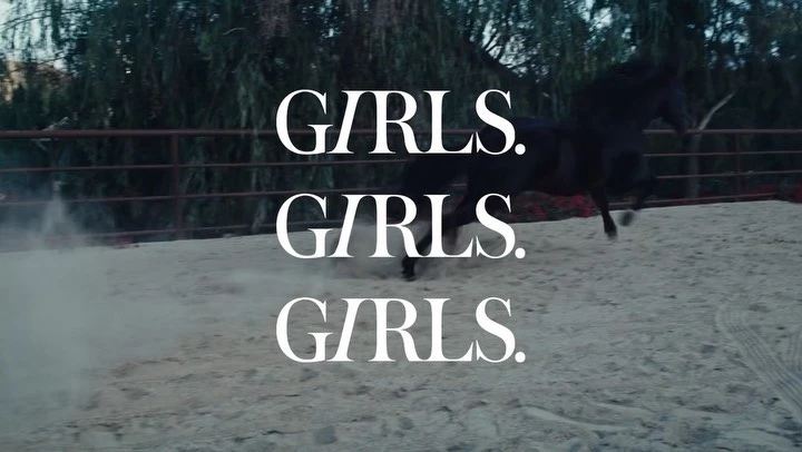 Dramatic shot of a black horse galloping in a sandy outdoor arena, framed by dark trees and overlaid with bold white text reading 'GIRLS'.