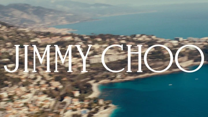 Overhead view of a coastal town with turquoise water and the 'Jimmy Choo' brand logo superimposed over the landscape.