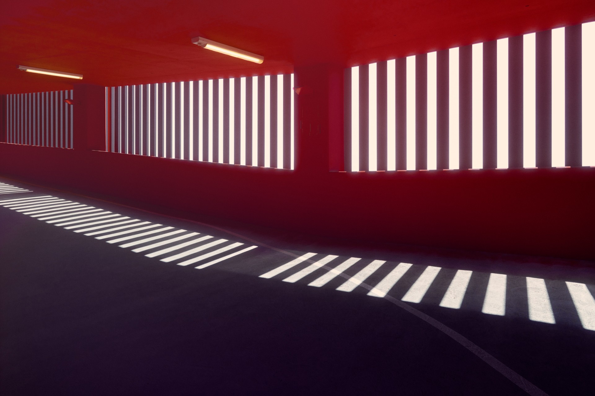 Illuminated corridor with red walls and bright, patterned light filtering through slatted windows, casting linear shadows on the floor.