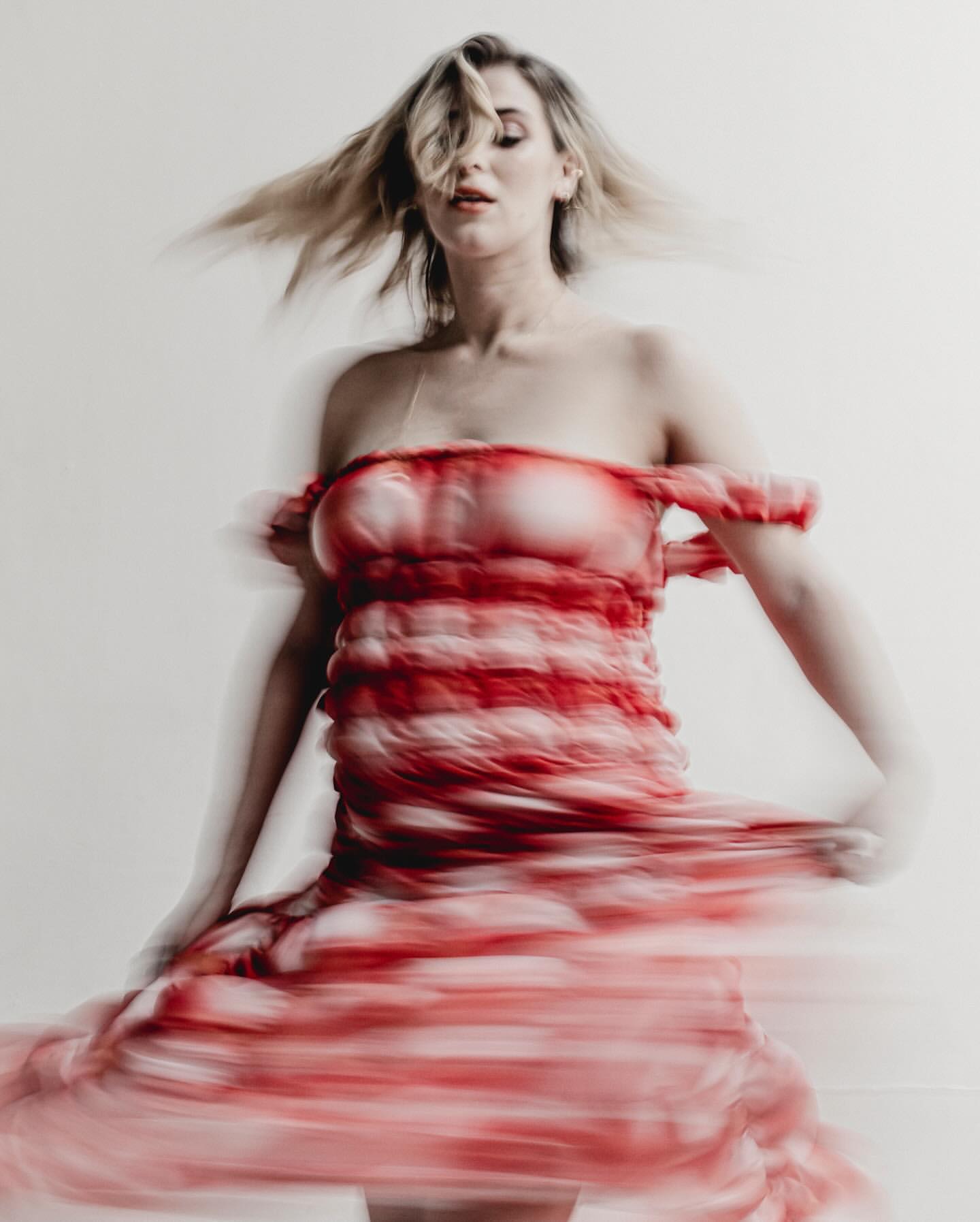 A woman with blonde hair wearing a red and white striped dress is photographed in motion against a plain white background, blurred movement.