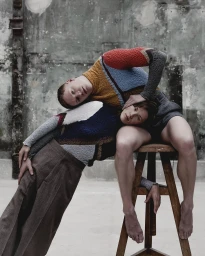 Two models posing together with a wooden stool against a weathered industrial concrete wall by Paul Phung
