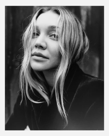 Close-up monochrome portrait of a woman with blonde hair and dark jacket against a dark background.
