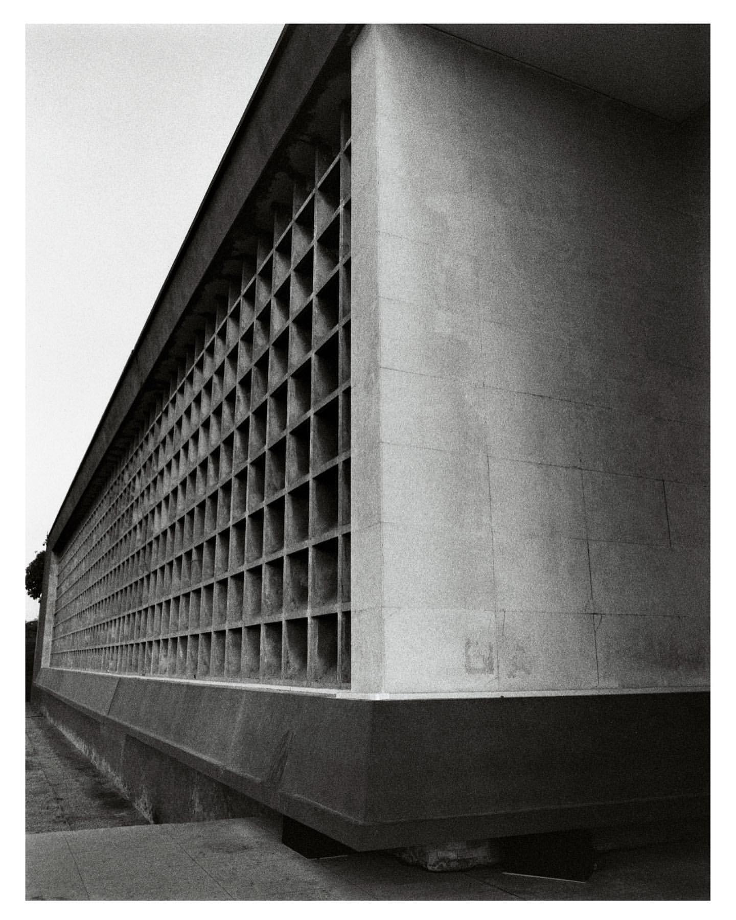 Architectural detail of a modern building featuring a repetitive grid pattern facade and textured concrete exterior in black and white.