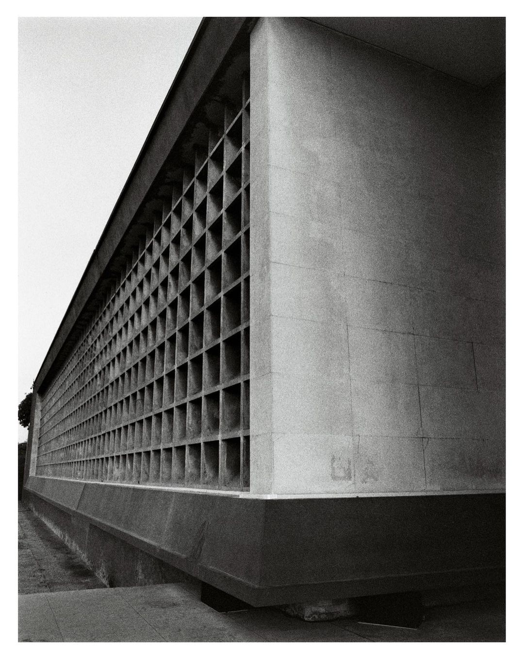 Black and white photograph of an architectural building exterior featuring a textured concrete facade and a repetitive geometric window pattern.
