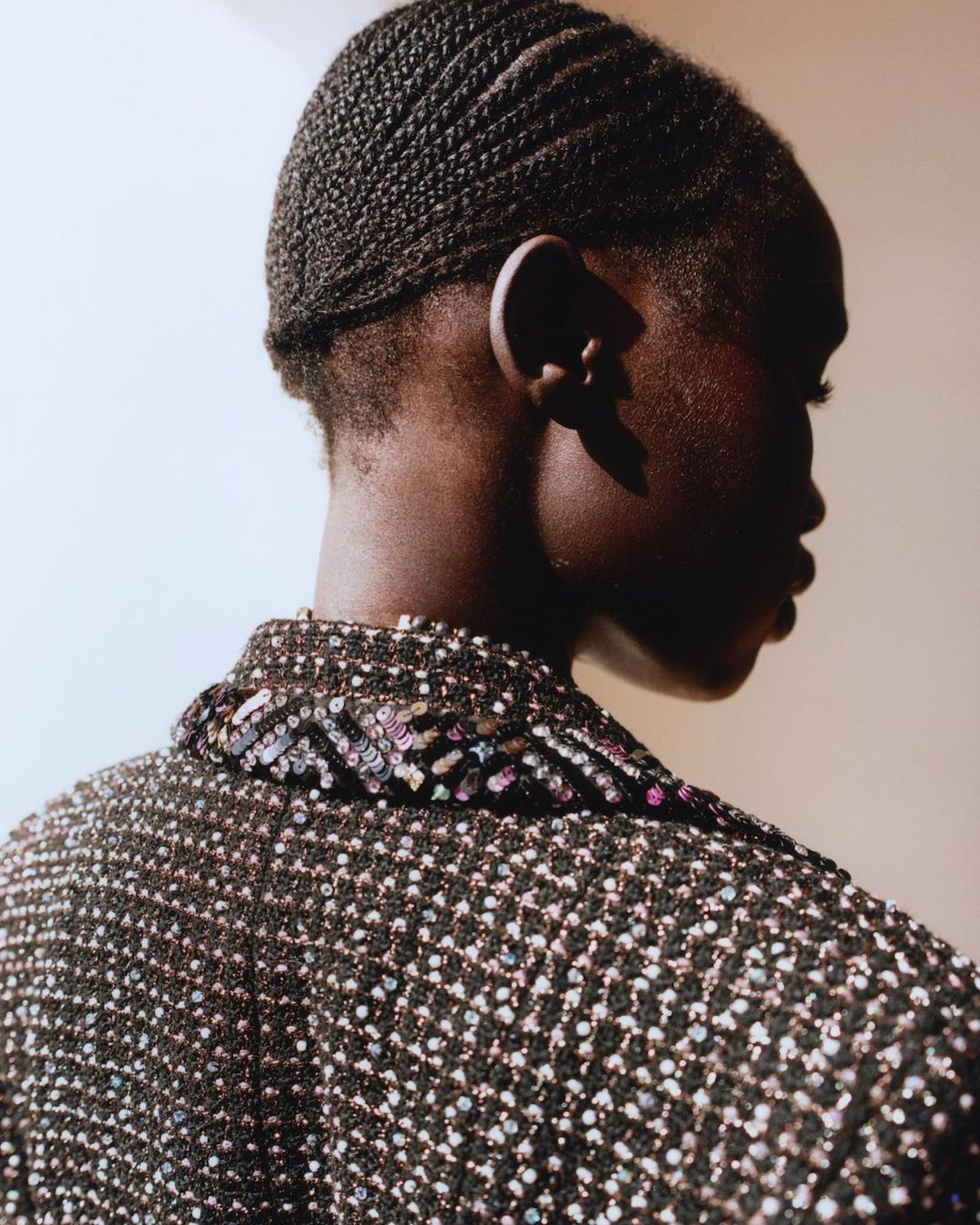 Profile portrait of a Black woman in a brown jacket with a patterned collar, showcasing her cornrow hairstyle and dark skin.