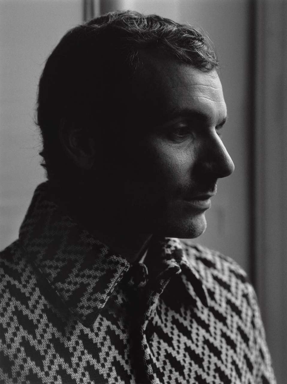 Monochrome portrait of adult male in patterned knit shirt, side profile with shadowed face in soft, neutral indoor light.