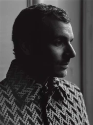 Monochrome portrait of a man in a patterned houndstooth jacket shot in profile by Paul Schmidt in Paris.