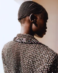 Close-up portrait of a Black model in profile wearing a heavily textured sequined jacket with cornrows hairstyle.