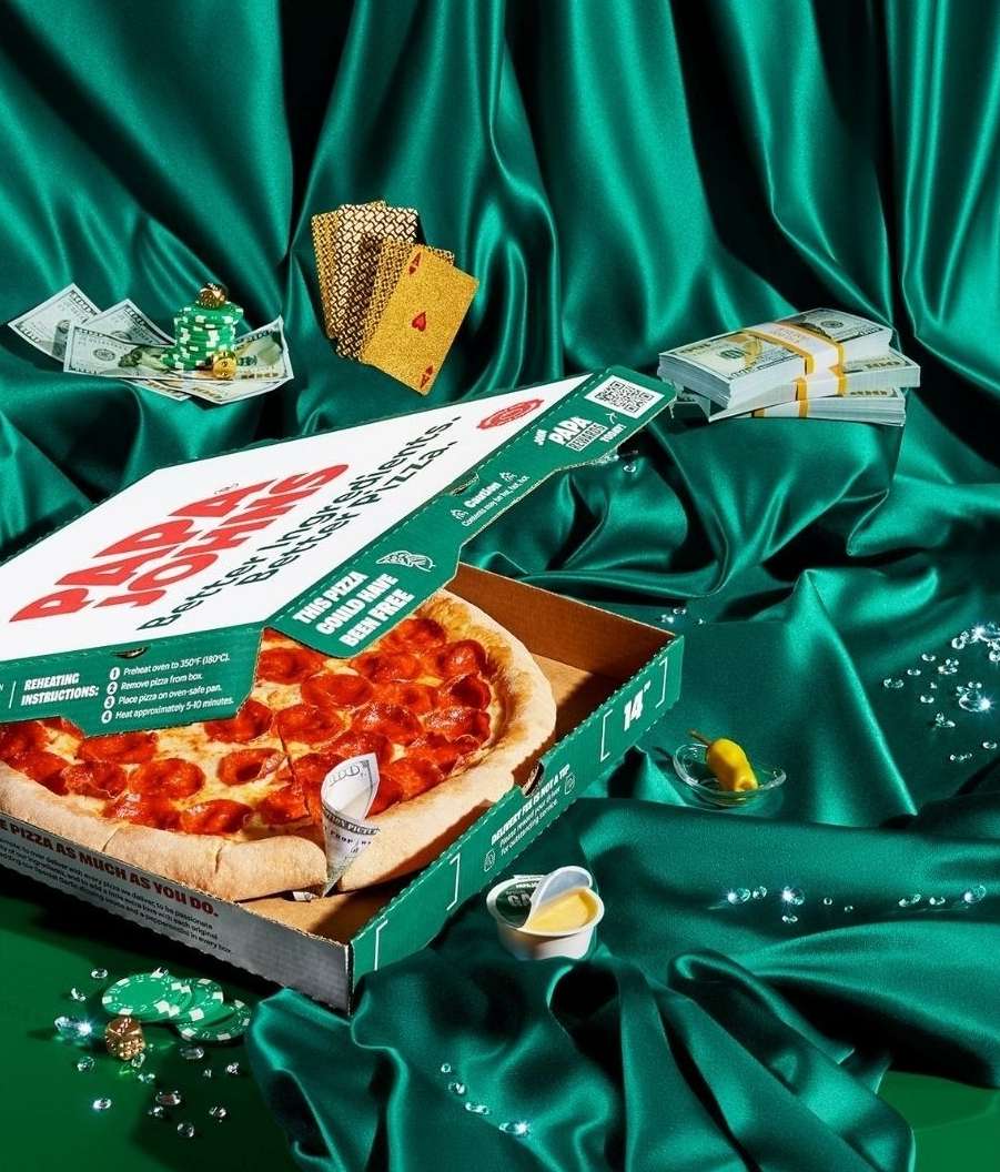 Overhead shot of a pepperoni pizza in an open pizza box, surrounded by money, poker chips, cards, and a small container of dipping sauce.