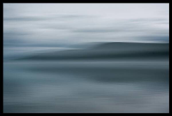 Abstract long exposure photograph of a dark shoreline and water under an overcast sky with motion blur.