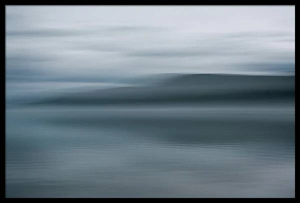 Abstract long exposure photograph of a dark shoreline and water under an overcast sky with motion blur.