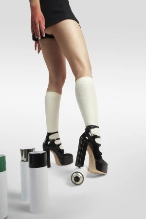 Close-up of a person wearing black shorts, white knee socks, and black platform heels standing on a spray paint can