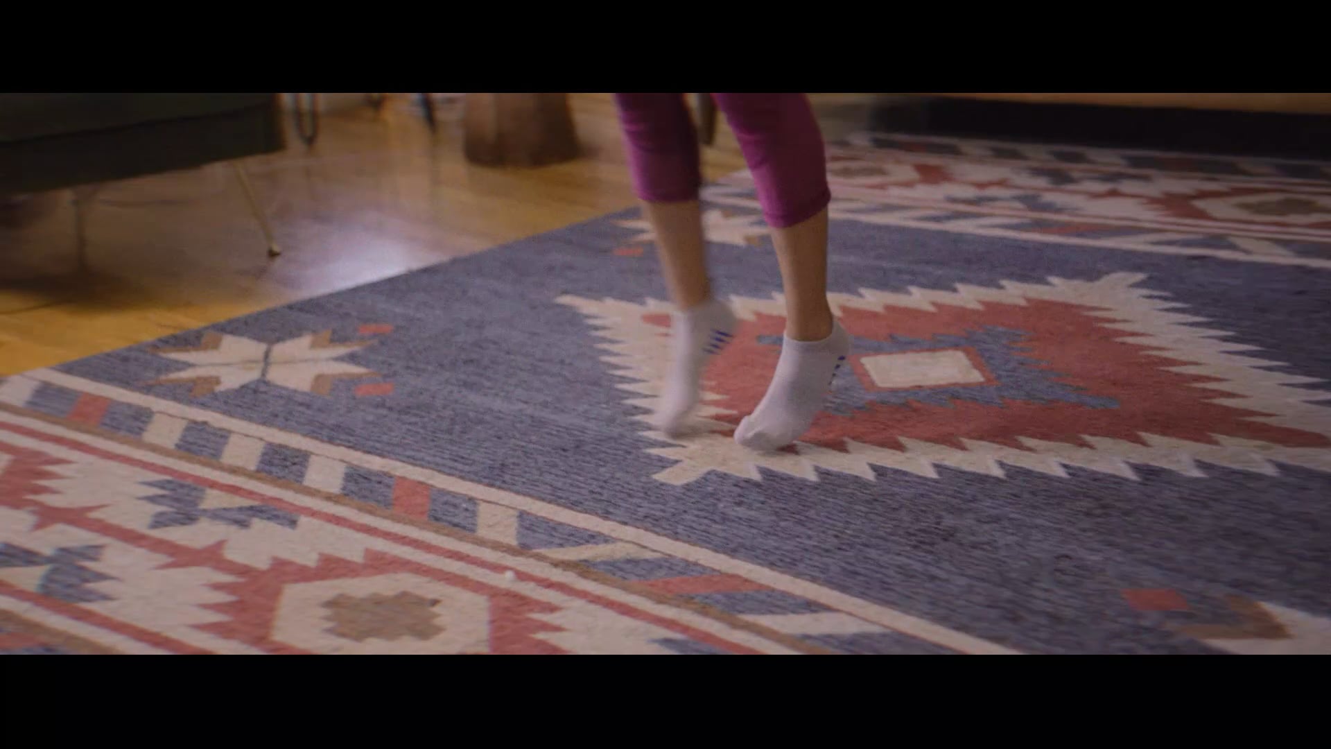 Close-up of a person jumping in mid-air wearing purple leggings and grey ankle socks over a patterned rug