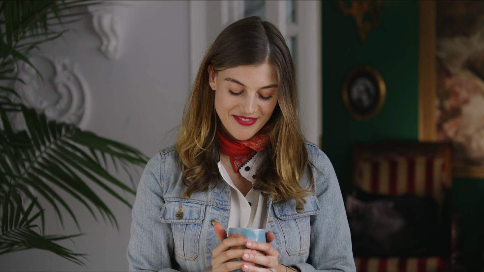 Woman in denim jacket holding a ceramic mug with a red bandana around her neck