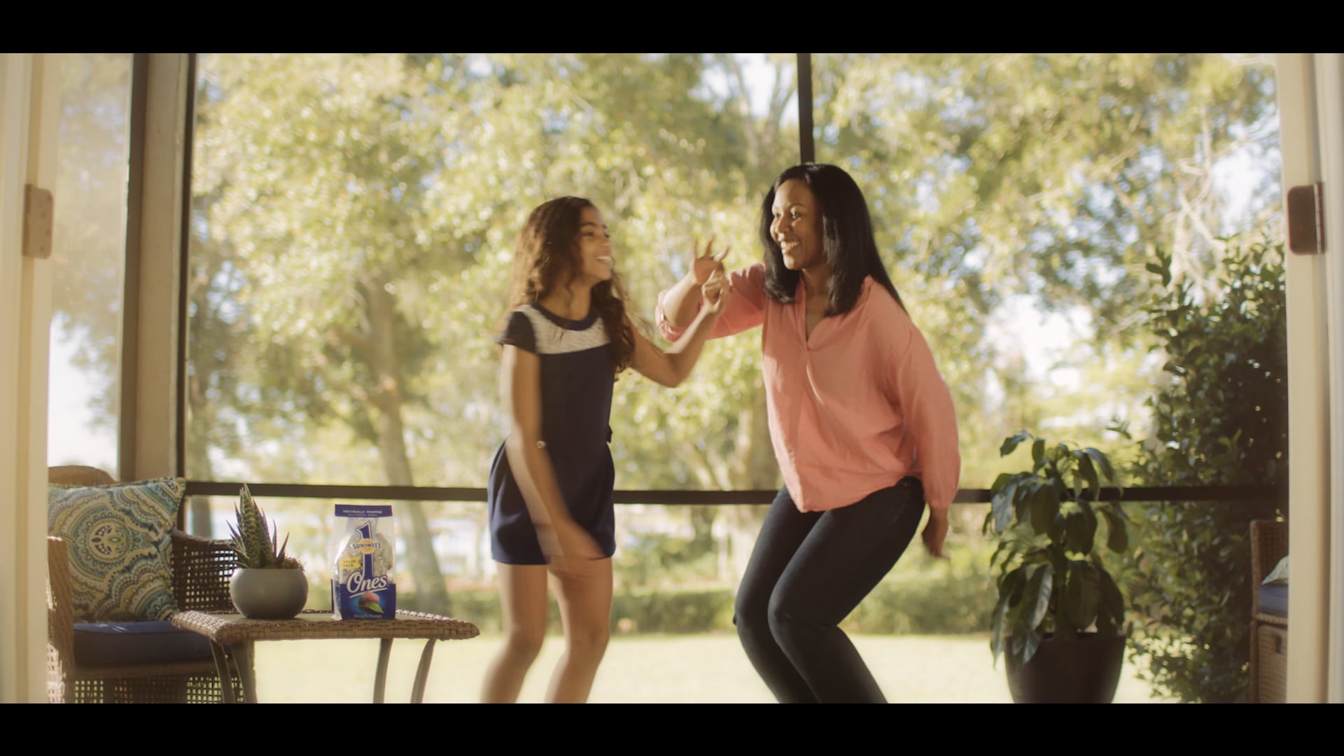 Mother and daughter smiling and dancing together on a screened porch with greenery visible outside
