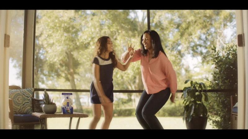 Mother and daughter smiling and dancing together on a screened porch with greenery visible outside