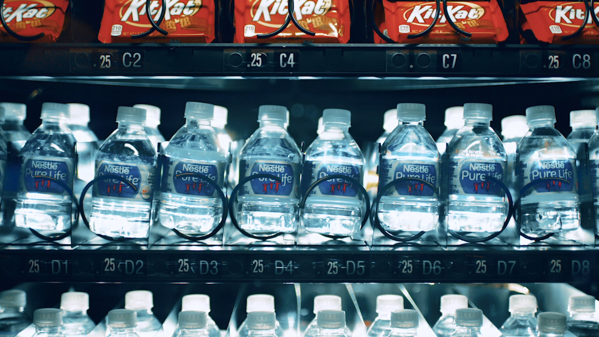 Rows of bottled water and packaged candy inside an illuminated vending machine, captured by Erin Collett
