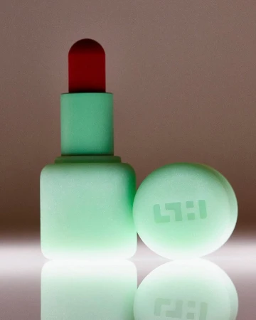 Mint green lipstick tube with a bright red tip and matching cap placed beside it against a gradient background.