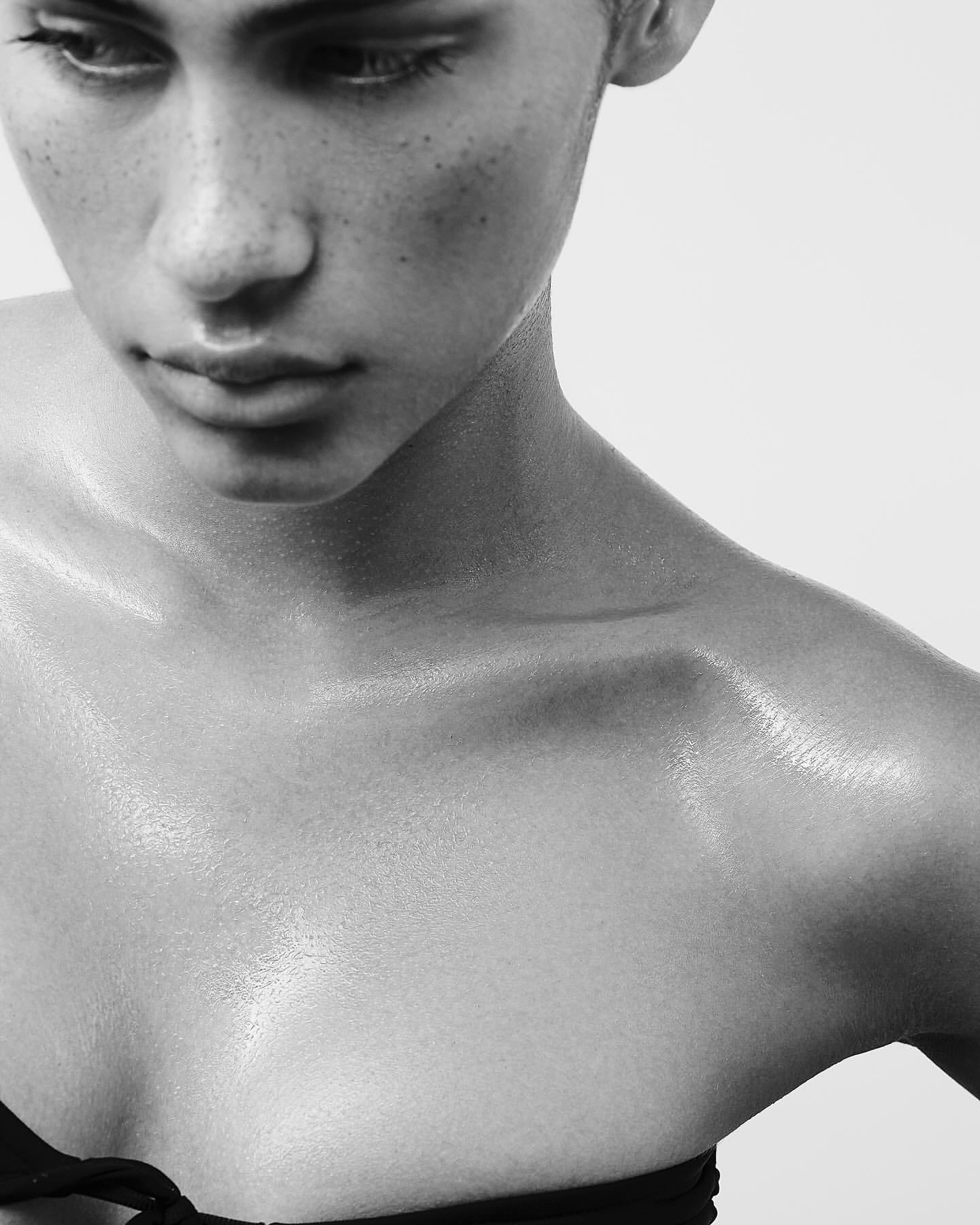 Close-up portrait of a young adult female with freckles and light skin, looking downward in a black and white photo. The woman has bare shoulders.