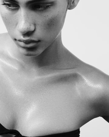 Close-up portrait of a young adult female with freckles and light skin, looking downward in a black and white photo. The woman has bare shoulders.