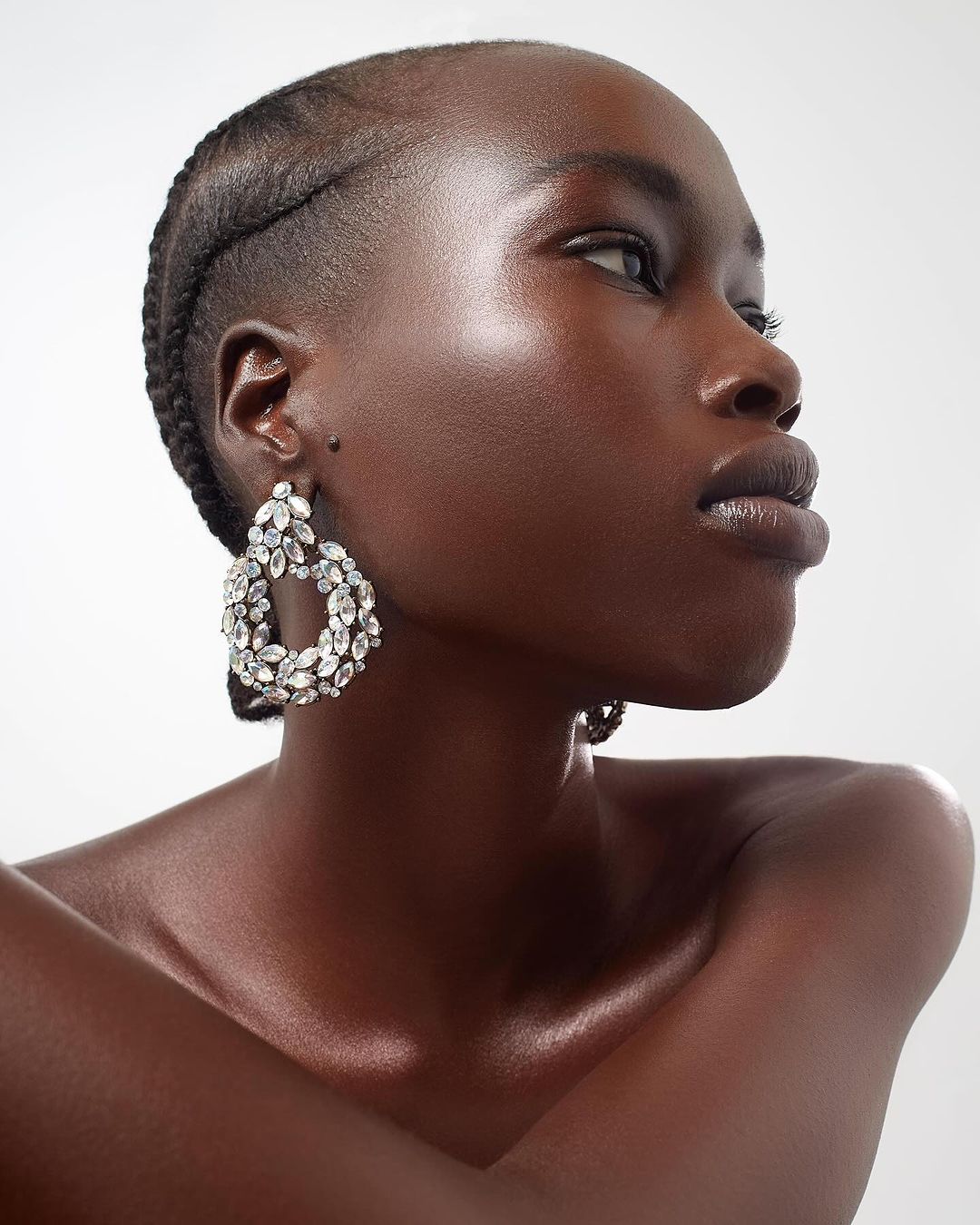 Headshot of a Black woman in a sleeveless top, with braided hair and dangling crystal earrings against a plain white background.