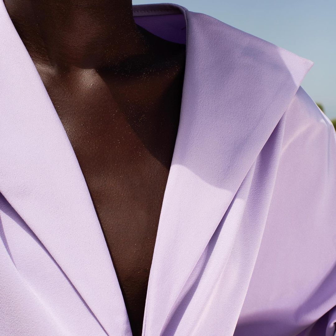 Close-up of a dark-skinned person wearing a light purple jacket, focusing on the texture and color of the clothing and skin.