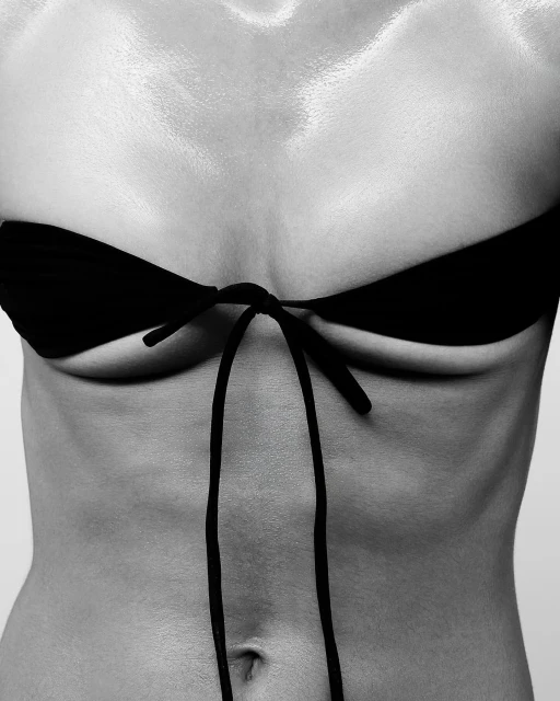 Close-up black and white studio shot of the bare chest and stomach of an adult woman in a black string bikini top.