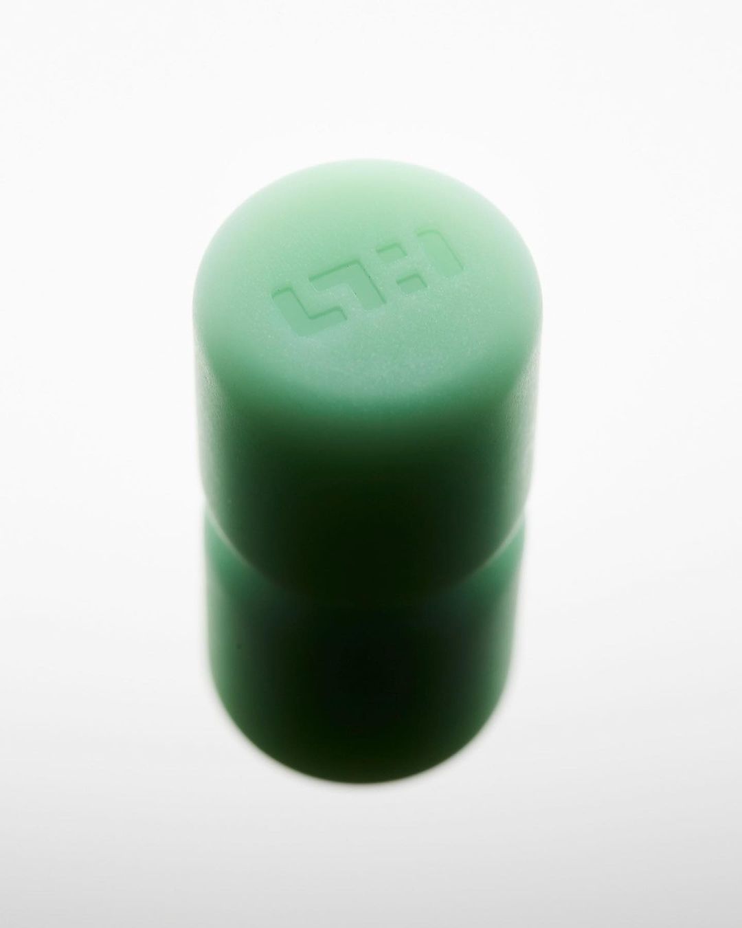 Close-up studio shot of a glossy green cylindrical object with rounded top, with embossed text on a bright white background.