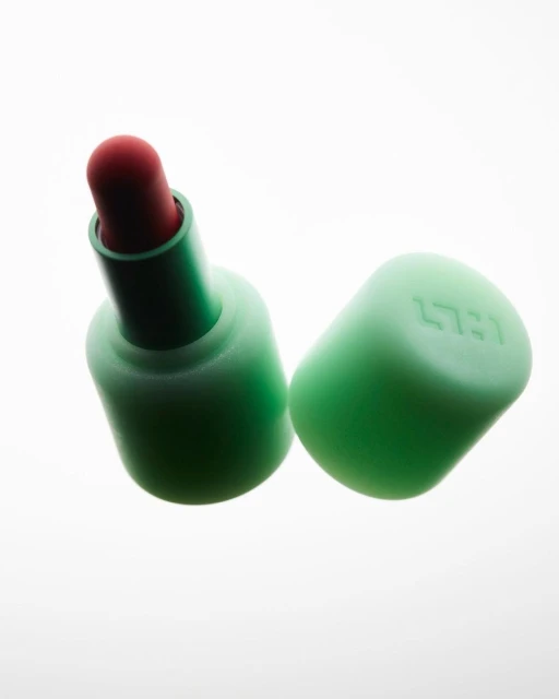 Red lipstick with a light green case and matching cap, photographed on a white surface.