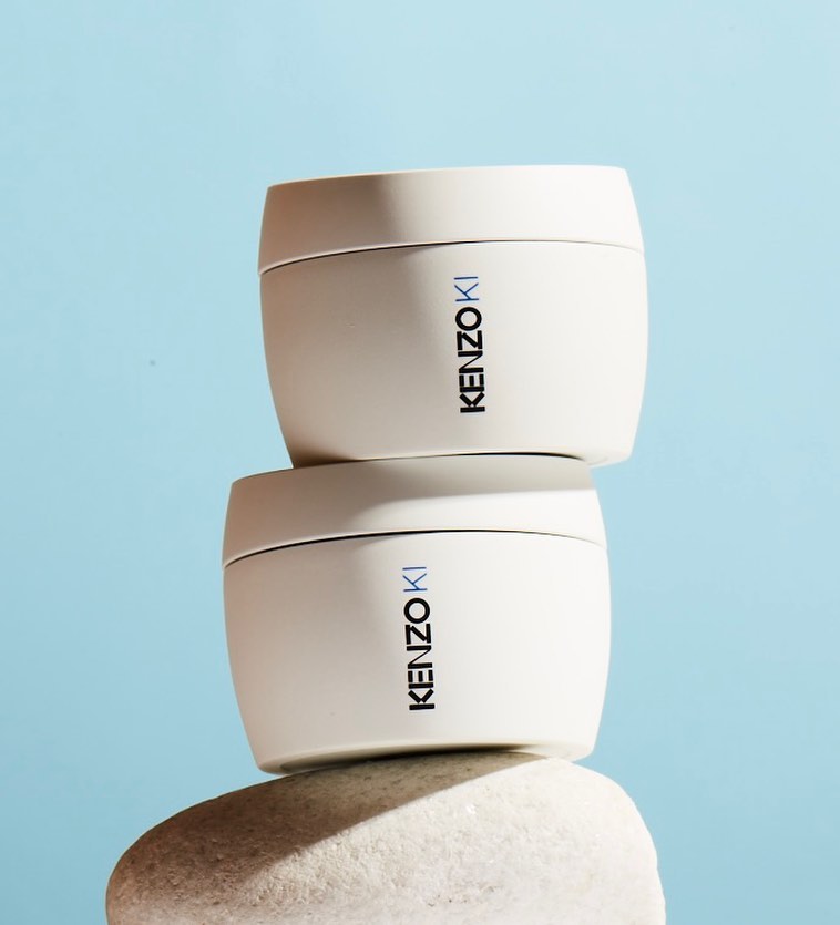Two stacked jars of KenzoKi skincare sit on a white stone against a light blue background, product shot for beauty and cosmetics.