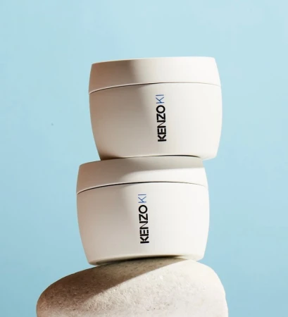 Two stacked jars of KenzoKi skincare sit on a white stone against a light blue background, product shot for beauty and cosmetics.