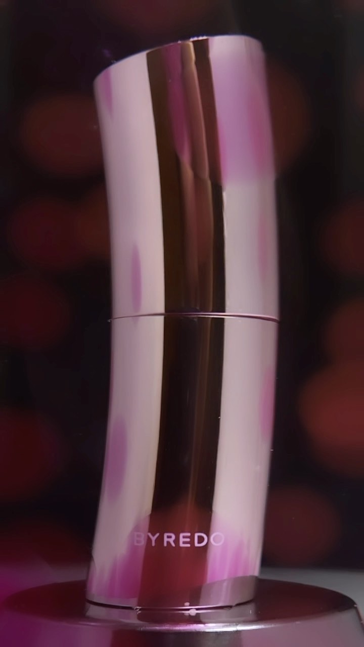 Close-up studio shot of Byredo lipstick with a rose gold casing, set against a blurred background with bokeh lights.