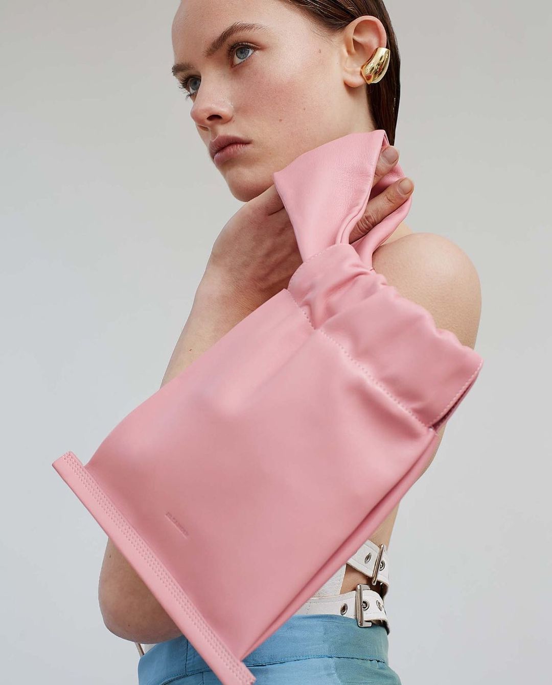 Fashion shot featuring a light-skinned adult woman with a short slicked-back hairstyle posing with a pink leather handbag.